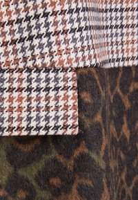 Vævet stof med et brunt, sort og hvidt hundetandsmønster, lagt over en mørkegrøn og brun leopardprinttekstur.