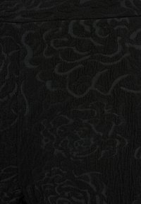 Černá texturovaná tkanina s jemným květinovým vzorem, která vykazuje různé odstíny černé, vytvářející hloubku a rozměr v designu.