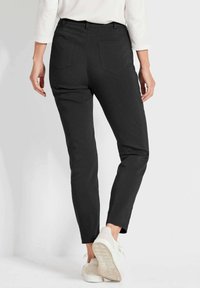 Schwarze taillierte Hose mit glatter Oberfläche, schlankem Schnitt und vier Taschen, kombiniert mit hellen Turnschuhen.