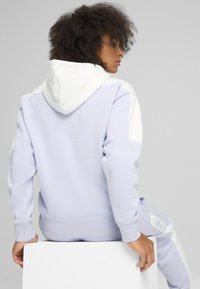 Felpa con cappuccio color lavanda chiaro con dettagli bianchi, tessuto morbido, vestibilità comoda e polsini a coste. Design semplice senza motivi evidenti.