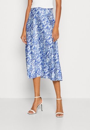 Blauwe midi-rok met patroon en een vloeiend ontwerp, uitgevoerd in een zachte stof en voorzien van een elastische tailleband. Gecombineerd met witte sandalen met bandjes en hak.