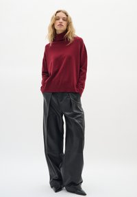 Pull roulé bordeaux associé à un pantalon large en cuir noir taille haute ; textures lisses et coupe ajustée remarquables.
