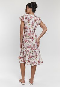 Robe fleurie avec des motifs roses et verts sur fond blanc, dotée de manches courtes à volants et d'une jupe évasée.