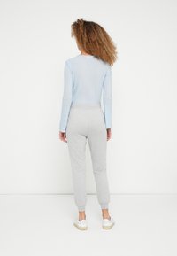Lichtblauw geribd shirt met lange mouwen, grijze taps toelopende joggingbroek en witte sneakers. Materialen zonder textuur, relaxte pasvorm, zichtbare stikdetails.