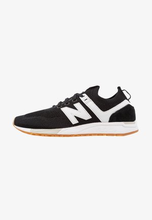 Black athletic shoes with mesh upper, white accents, and black suede heel. Features a rubber sole and prominent "N" logo.