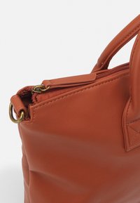 Brun læder tote taske med lynlåslukning, afrundede håndtag og metaldetaljer. Har en glat overflade og et minimalistisk design.