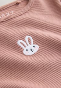 Tricou roz din bumbac cu textură tip reţea, având pe centrul pieptului o față de iepure brodată albă, cu ochi negri și obraji roz.