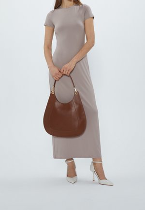 Borsa hobo in pelle marrone con dettagli dorati, caratterizzata da una forma arrotondata e una texture liscia. Il modello indossa un abito taupe aderente e tacchi bianchi.