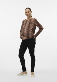 Blusa de leopardo marrón de manga larga, corte relajado, combinada con jeans ajustados negros y cómodas bailarinas claras.