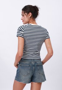 Navy and white striped fitted t-shirt with short sleeves, paired with high-waisted, frayed hem denim shorts. Simple and casual design.
