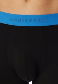 Boxer da uomo neri con un elastico blu in vita che presenta la scritta "SCHIESSER" in un motivo a contrasto. Realizzati in un tessuto morbido e elasticizzato.