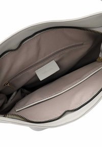 Binnenkant van de witte leren handtas heeft een beige stoffen voering, één ritsvak en twee compartimenten met een zwarte ritsdetail. Label zichtbaar.