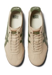 Beige leather sneakers with green accents, featuring a lace-up design, textured soles, and the "Onitsuka Tiger" logo on the tongue.