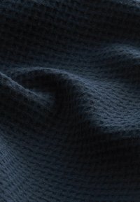 Tejido de color azul oscuro con una textura y patrón tejido, que exhibe sutiles ondulaciones y profundidad. La superficie parece suave y acogedora.