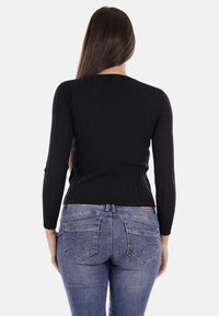 Maglietta nera a maniche lunghe con costine abbinata a jeans skinny di medio lavaggio con cuciture curve sulle tasche posteriori. Design liscio e aderente.