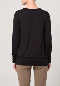 Svart långärmad topp i mjukt tyg, med rund halsringning och avslappnad passform, kombinerad med ljusbruna byxor.