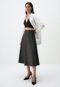 Grijze, knie-lange rok van gestructureerde stof, gecombineerd met een zwarte crop top en een witte overhemd, aangevuld met zwarte hoge hakken.