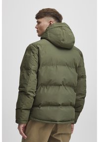 Olive green puffer jacket with a hood, quilted design, and long sleeves. Smooth texture and elastic cuffs complete the functional look.