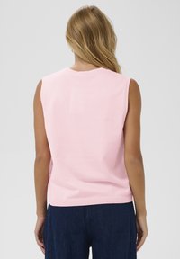 Rāvējslēdzēja rozā džemperis ar īsām piedurknēm, izgatavots no mīksta adījuma materiāla, ar noapaļotu apkakli un ribotu apakšmalu. Aizmugures skats parāda gludu tekstūru.