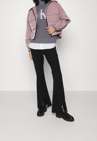 Pink semi-opaque jacket, gray ribbed sweater with logo, white shirt, black flared pants with side slits, and black ankle boots.