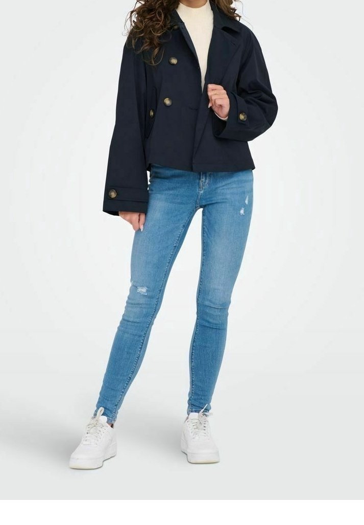 Chaqueta corta de doble botonadura en color navy con grandes botones, combinada con jeans ajustados desgastados de color azul claro y zapatillas blancas.