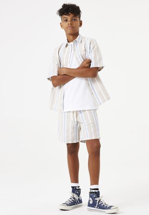 Korte mouwen gestreepte shirt in beige en blauw, gecombineerd met bijpassende shorts. Voorzien van knoopsluiting en een verstelbare taille met trekkoord. Gestyleerd met blauwe hoge sneakers.