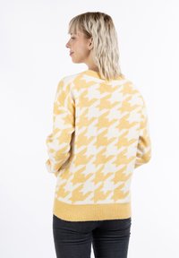 Sárga és krém houndstooth mintázatú pulóver, kerek nyakkivágással és bordázott szegéllyel, puha kötött anyagból készült.