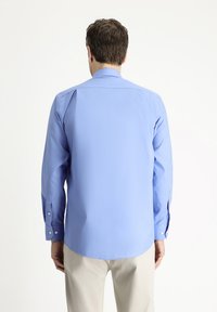 Camisa de vestir azul claro con mangas largas, puños con botones, un cuello clásico y un ajuste liso y entallado. La vista trasera muestra un dobladillo redondeado.