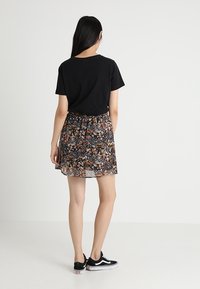 Svart t-shirt med kort ärm kombinerad med en blommig kjol med svart bakgrund och färgglada små blommor. Bärs med svarta sneakers.