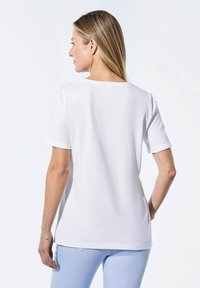 Witte T-shirt met korte mouwen, zachte stof, ronde hals, relaxed fit, zichtbare stiksels, gedragen met lichtblauwe broek, minimalistisch ontwerp, geen patronen.