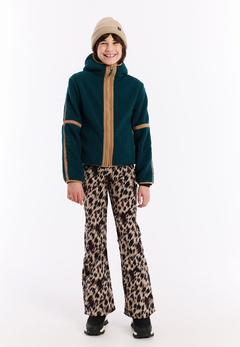 Tyrkysová fleecová bunda s béžovým zipsom a bočnými akcentmi, spárovaná s rozšírenými nohavicami s leopardím vzorom a béžovým pleteným čiapkom. Viditeľná čierna obuv.