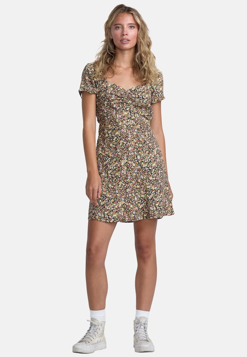 Zwart bloemenprint jurk met korte pofmouwen, gerimpelde voorkant en een uitlopende zoom. Gestyled met witte sneakers en enkelsokken.