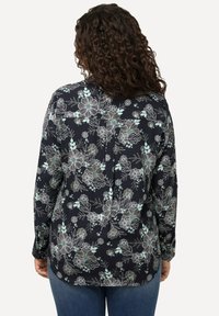 Camicia a maniche lunghe con motivo floreale in blu navy con accenti azzurri, dotata di una spalla posteriore abbottonata e orlo leggermente curvo. Realizzata in tessuto leggero.