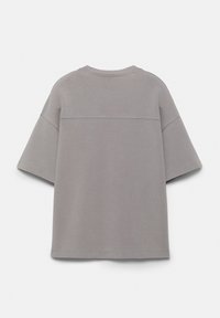 Chemise grise surdimensionnée à manches courtes vue de dos, avec des épaules tombantes et une couture horizontale traversant le haut du dos.