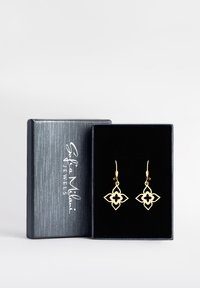 Guldörhängen i en blommönsterdesign med utskurna mönster, visade i en grå låda klädd med svart sammet. Varumärkeslogotyp synlig på lådan.