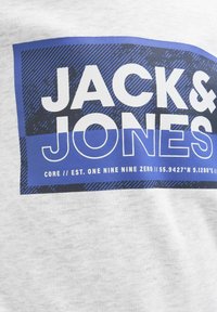 T-shirt grigio con una grafica rettangolare blu che presenta il testo "JACK & JONES" in bianco. Include coordinate e un motivo testurizzato sullo sfondo.