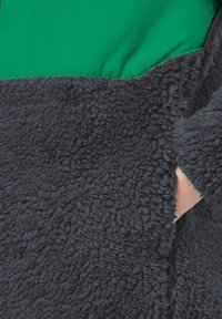Vlooizachte donkergrijze fleecestof met een gestructureerd oppervlak; heeft een groene nylon bovenkant en een zijzakopening.
