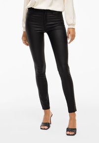 Svarta läderleggings med smal passform, hög midja och slät yta, kombinerat med svarta öppna klackskor.