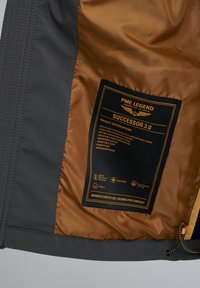 Gray softshell jacket interior with a gold lining, featuring a care label with specifications and symbols for waterproof and breathable properties.