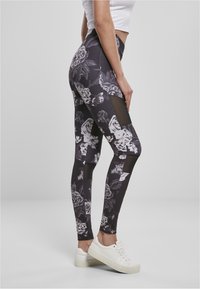 Svarta blommiga leggings med genomskinliga meshnätspaneler, åtsittande design och hög midja, parat med vita sneakers.