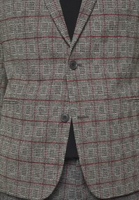 Grijze houndstooth blazer met een rood ruitpatroon, voorzien van twee zwarte knopen en een enkele zak, gemaakt van een textuurstof.