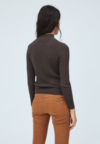Brauner, gerippter Pullover mit langen Ärmeln und hohem Kragen. Kombiniert mit orange-braunen Hosen, die eine schmale Silhouette betonen.