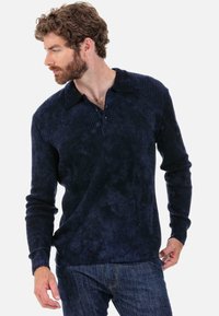 Marineblaue, gerippte Langarmshirt mit Knopfleiste und Kragen. Weiche Textur mit enganliegenden Bündchen und entspannter Silhouette. Jeans sichtbar.