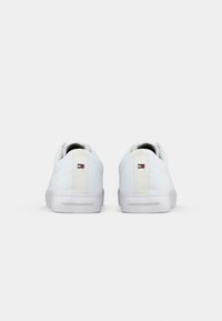 Paire de baskets basses blanches avec le logo Tommy Hilfiger rouge, blanc et bleu sur le talon et le nom de la marque embossé sur la semelle.