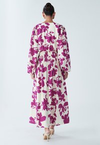 Pikk kleit, mille külge jääb valge taust suuremate lilla lillemustritega, elastse vöökohaga ja pikkade varrukatega. Sile kangastekstuur.