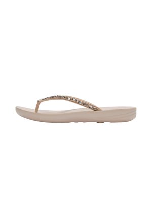 Beige teenslipper met een licht verhoogde zool en een met juwelen versierde band, zijaanzicht op een witte achtergrond.