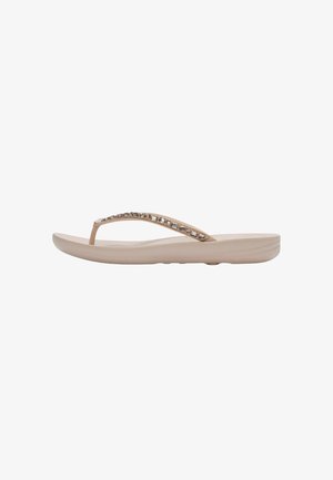 Beige teenslipper met een licht verhoogde zool en een met juwelen versierde band, zijaanzicht op een witte achtergrond.