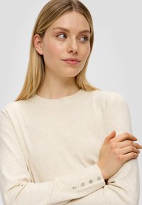Helle beige Strickjacke mit langen Ärmeln, rundem Ausschnitt und Knopfakzenten an den Bündchen. Weicher, strukturierten Stoff mit lockerer Passform.