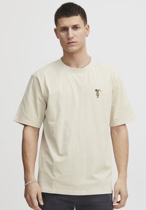 Beige színű pamut póló rövid ujjakkal, apró hímzett mintával a mellkason. Egyszerű és laza fazon.