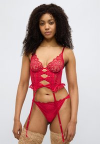 Σετ εσωρούχων από κόκκινη δαντέλα που περιλαμβάνει κορσέ με διαφανή πάνελ, λουλουδάτα μοτίβα, κυματιστές άκρες και ρυθμιζόμενους τιράντες, συνοδευόμενο από ταιριαστό σλιπ.